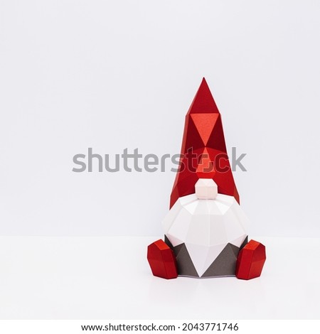Cute Christmas gnome in red pointed hat with white beard, paper polygonal figure dwarf, New Year holiday concept, minimal style  background with copy space. 