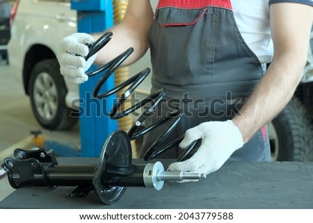 Spare parts for the car. A spring is in the hands of an auto mechanic, a shock absorber strut is lying on the desktop. The specialist checks the compatibility of the spring part and the shock absorber Royalty-Free Stock Photo #2043779588