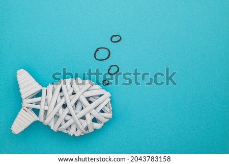 Fish made with weaved wood on blue background with drawing of bubbles. Concept for ocean life. Copy space