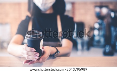 Barista in apron and face mask standing behind counter bar ready to give Coffee Service at the modern coffee shop, Modern café business, Social distancing concept. Holiday concept with coffee