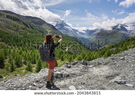 A woman hiker taking a photo with her mobile phone of Switzerland's most beautiful mountain, the Matterhorn, on a sunny summer day.