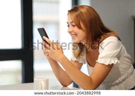 Happy woman reading text on smart phone at home