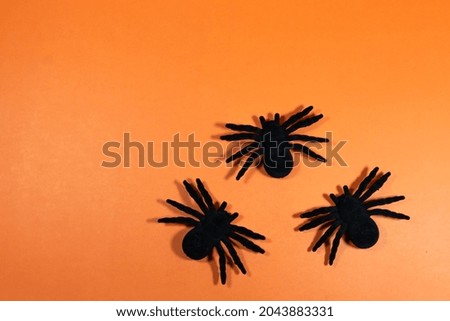 Three Halloween spiders, on orange background with copy space.