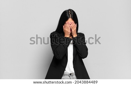 young hispanic businesswoman feeling sad, frustrated, nervous and depressed, covering face with both hands, crying