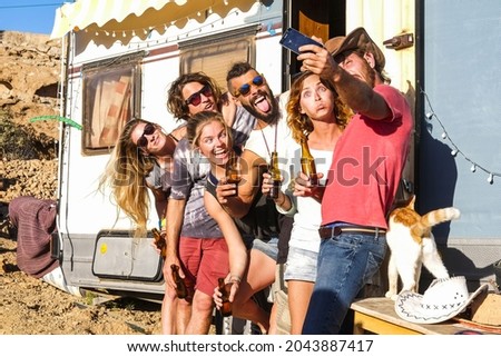 Group of young people friends taking selfie picture using mobile phone outside caravan. Group pf people making funny faces and holding beer bottle while taking selfie.