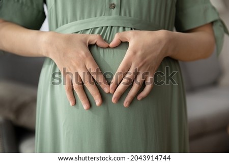 I love you my baby. Cropped close up of affectionate future mother make tender heart shape of united fingers on big pregnant belly. Loving expectant woman in anticipation wait for beloved wanted child Royalty-Free Stock Photo #2043914744