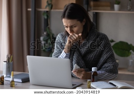 Unhealthy businesswoman wrapped in plaid working on laptop at home office, feeling unwell, sick young woman freelancer or student sitting at desk with medications, suffering from flu or virus Royalty-Free Stock Photo #2043914819