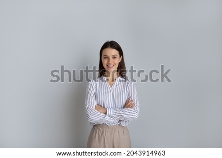 Portrait confident smiling young woman with arms crossed isolated on grey studio background, happy successful businesswoman entrepreneur or student standing with folded hands looking at camera