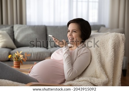 Enjoying pregnancy. Happy young future mom send voice message record audio blog on cell devoted to anticipation parenthood maternity. Positive mother to be dictate vocal letter to beloved wanted child