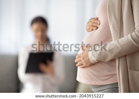 Preparing for baby birth. Close up of woman expecting baby having appointment with doctor at antenatal clinic prenatal healthcare center. Focus on young female holding hands on baby bump in doc office Royalty-Free Stock Photo #2043915227