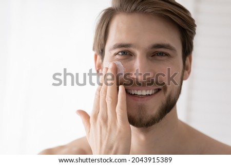 Close up portrait handsome 30s man applying facial cream smile look at camera, after shave beauty skincare products for smooth healthy moisturizing hydrated skin, skin-care cosmetics for men concept Royalty-Free Stock Photo #2043915389