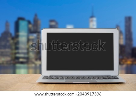 A laptop with a blank screen with a blurry city in the background. Paste your own image on the screen for a personalized picture