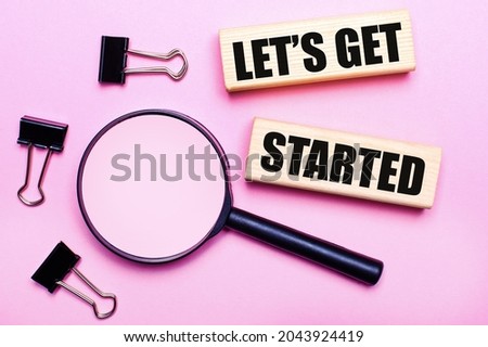 On a pink background, a magnifier, black paper clips and wooden blocks with the text LET IS GET STARTED. Business concept