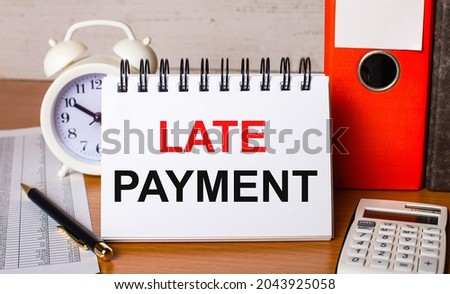 On the table are reports, a white alarm clock, a calculator, folders for papers, a pen and a white notebook with the LATE PAYMENT. Business concept Royalty-Free Stock Photo #2043925058
