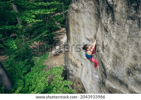 Young female rock climber climbing with rope on a rocky wall