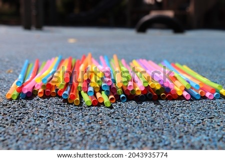 Selective focus. Colorful plastic drinking straws lying flat on blue rubber ground. Blurred playground in the background.