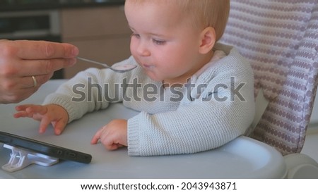 Caucasian Married Man Spoon Feeding Adorable Caucasian Baby Girl Watching Cartoon Film on Smarthphone