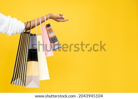 Sale offer. Black Friday. Shopping discount. Closeup of Afro woman hand holding purchase bags isolated on orange empty space background. Royalty-Free Stock Photo #2043945104