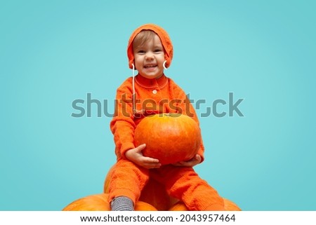 Kid girl in an orange suit sits on a big Halloween pumpkins and holding little pumpkin with copy space. place for text 