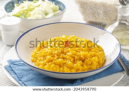 Italian dinner with risotto alla milanese and fresh salad. Italian dish made from saffron, rice, butter, hard cheese and vegetable broth. Raw arborio rice on background. White table. Royalty-Free Stock Photo #2043958790