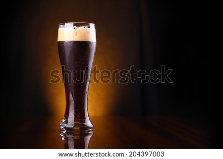 Tall glass of dark beer over a dark background lit yellow Royalty-Free Stock Photo #204397003