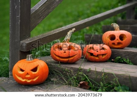 Pumpkins with carved faces and various emotions stand on the steps of an old wooden staircase near the house. Traditions of celebrating Halloween. Surprised, laughing, angry, squinting pumpkins