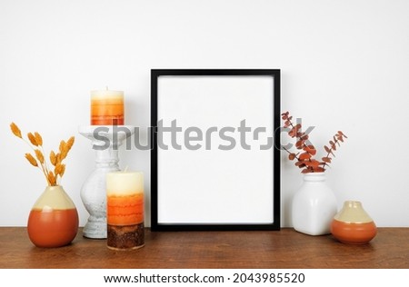 Mock up black frame with fall branches and decor on a wood shelf. Autumn concept. Portrait frame against a white wall.