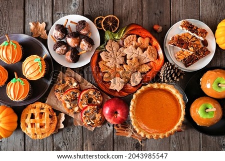 Autumn desserts table scene with a variety of sweet fall treats. Above view over a dark wood background.