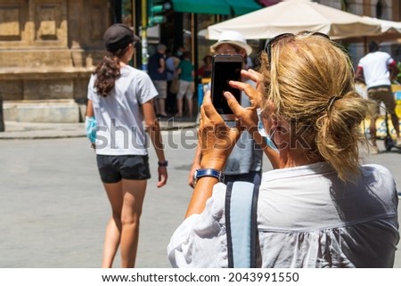 Mature woman taking a picture of a city of Palermo, Vigliena. Female doing a photo on a smartphone. Tourist concept.