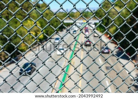 View of blurry highway traffic seen through chain link fence from overpass.