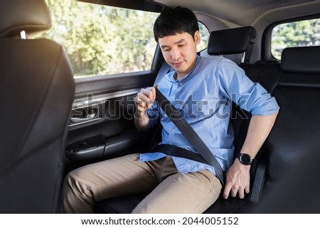 young man fastening a seat belt while sitting in the back seat of car  Royalty-Free Stock Photo #2044005152