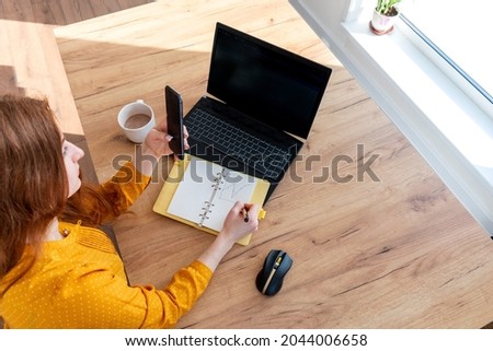 Young business woman is using the computer and talking on the phone. Female girl looks into a laptop computer. Live broadcast concept. Comfort zone in the house.