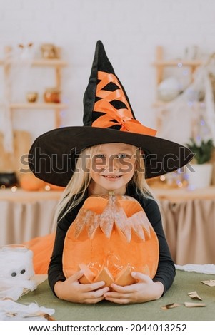 portrait a smiling blonde girl of European appearance in a huge witch hat hugs a large pumpkin lantern. halloween concept. High quality photo