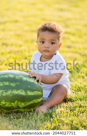 a little swarthy girl in white clothes eats a watermelon on a green lawn. picnic in the park. happy childhood. space for text. High quality photo