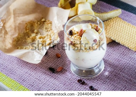 Delicious and healthy yogurt dessert with banana, biscuits and nuts close-up.