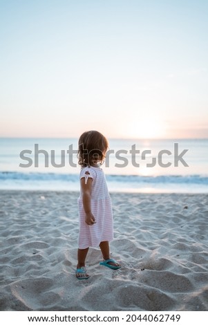 girl from behind and a white dress standing on a summer beach looking at sunset