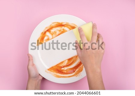 Woman using yellow cleaning sponge to clean up and washing food stains and dirt on white dish after eating meal. Royalty-Free Stock Photo #2044066601