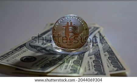 Bitcoin coin on stand stands on dollar bills on white background.