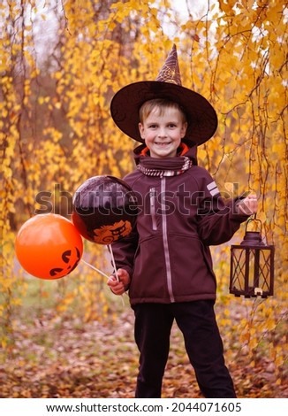 boy in wizard hat holding orange and black balloons and a vintage lantern in his hand, halloween celebration, autumn background 