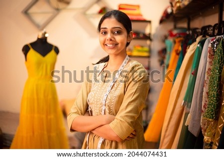 Portrait of Young happy indian woman, fashion designer tailor standing with crossed arms, measurement tape in garment workshop, seamstress, tailoring clothing on mannequin in  studio. skill india Royalty-Free Stock Photo #2044074431