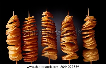 Yummy traditional Korean street food twister fries or twist potatoes on wooden skewers against black background Royalty-Free Stock Photo #2044077869