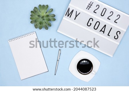 Open blank notebook page, pen, coffee cup, lightbox with My Goals text on office desk - top view. Plans for the coming year concept