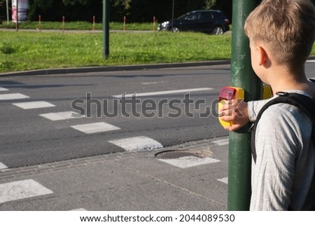 Schoolboy near pedestrian crossing and presses yellow device with button on demand on traffic light