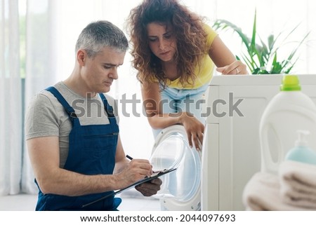 Technician performing a check-up on a washing machine, he is writing on a clipboard, repair service concept Royalty-Free Stock Photo #2044097693
