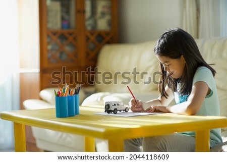 Asian girl child drawing with a pencil on paper under sun.Shadow draw concept.Cute young female draw in the living room.Homeschooling.Homeschool.Vehicle or transportation drawing hobby.