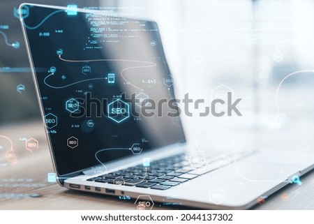 Close up of laptop computer with abstract glowing SEO interface with icons on blurry background. Search engine optimization and coding concept. Double exposure