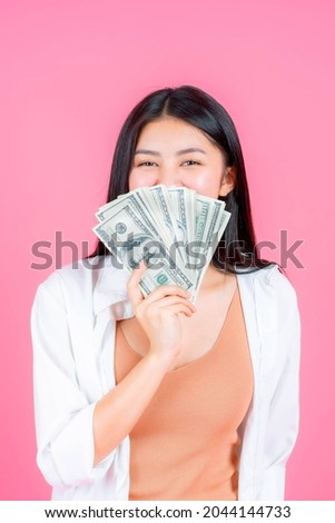 Successful beautiful Asian business young woman cute girl holding money US dollar bills in hand isolated on pink background , business concept
