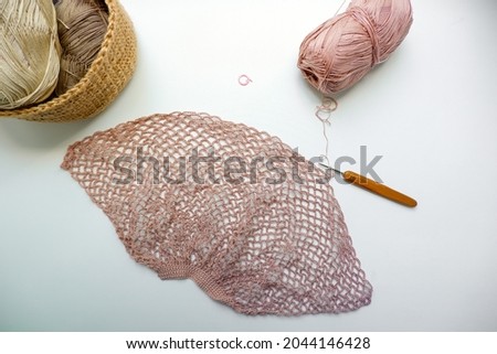 The process of creating a string bag. A skein of yarn of a delicate pink color, a knitting hook and a basket with yarn on a white background. The concept of zero waste. Photo from above.