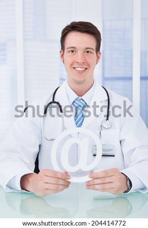 Portrait of young male doctor holding internet symbol at desk in clinic