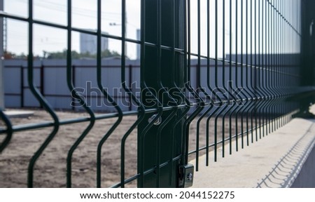Steel lattice green fence with wire. Fencing. Grid industrial wire fence panels, pvc metal. Installation of sectional fencing. Welded mesh fence. Installation of a grid for fencing the territory Royalty-Free Stock Photo #2044152275